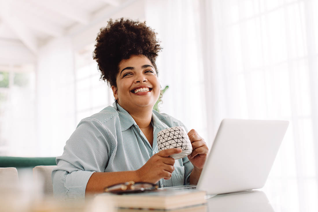 woman smiling while drinking coffee and working on her laptop